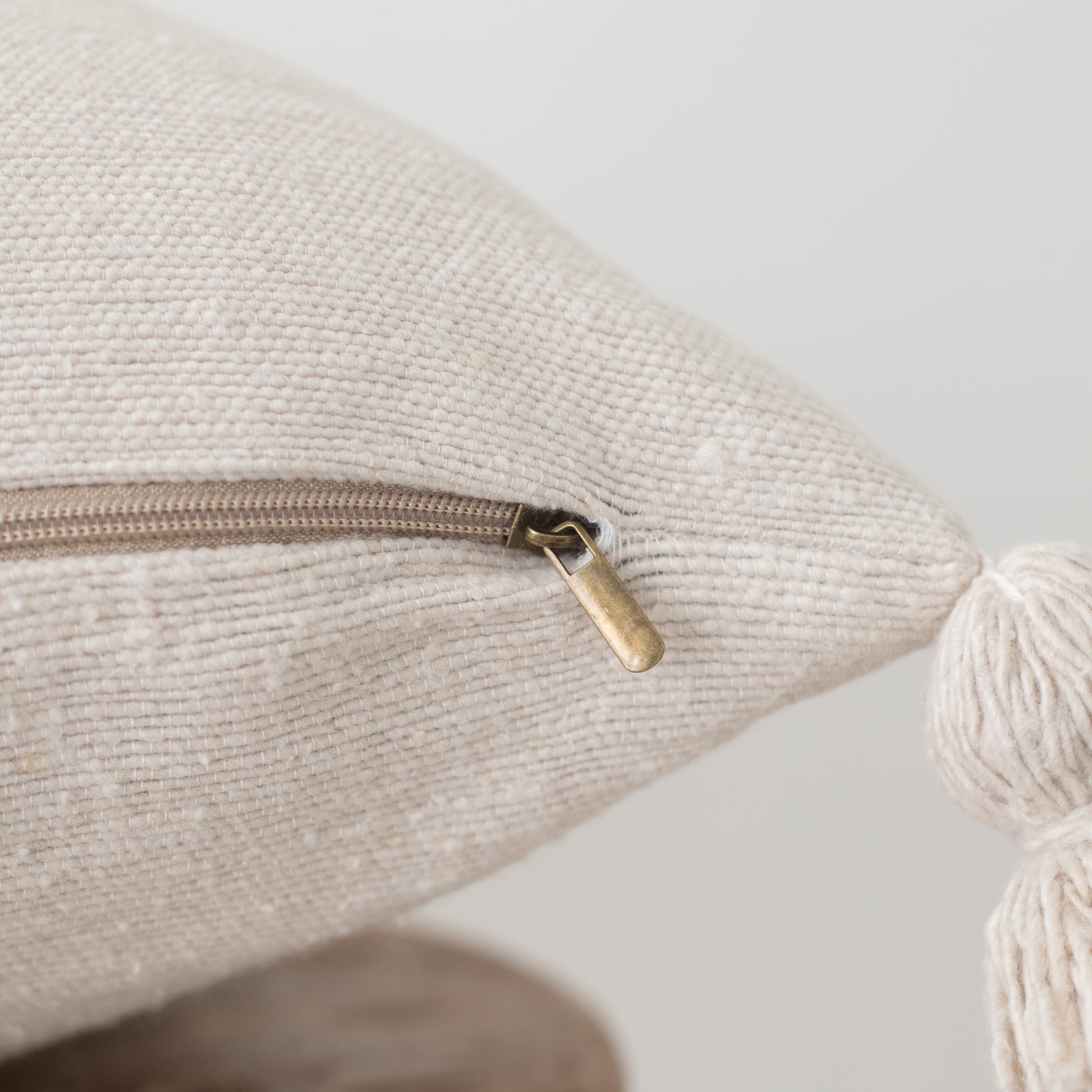 Cream textured pillow with side zipper and tassel detail, close-up view.
