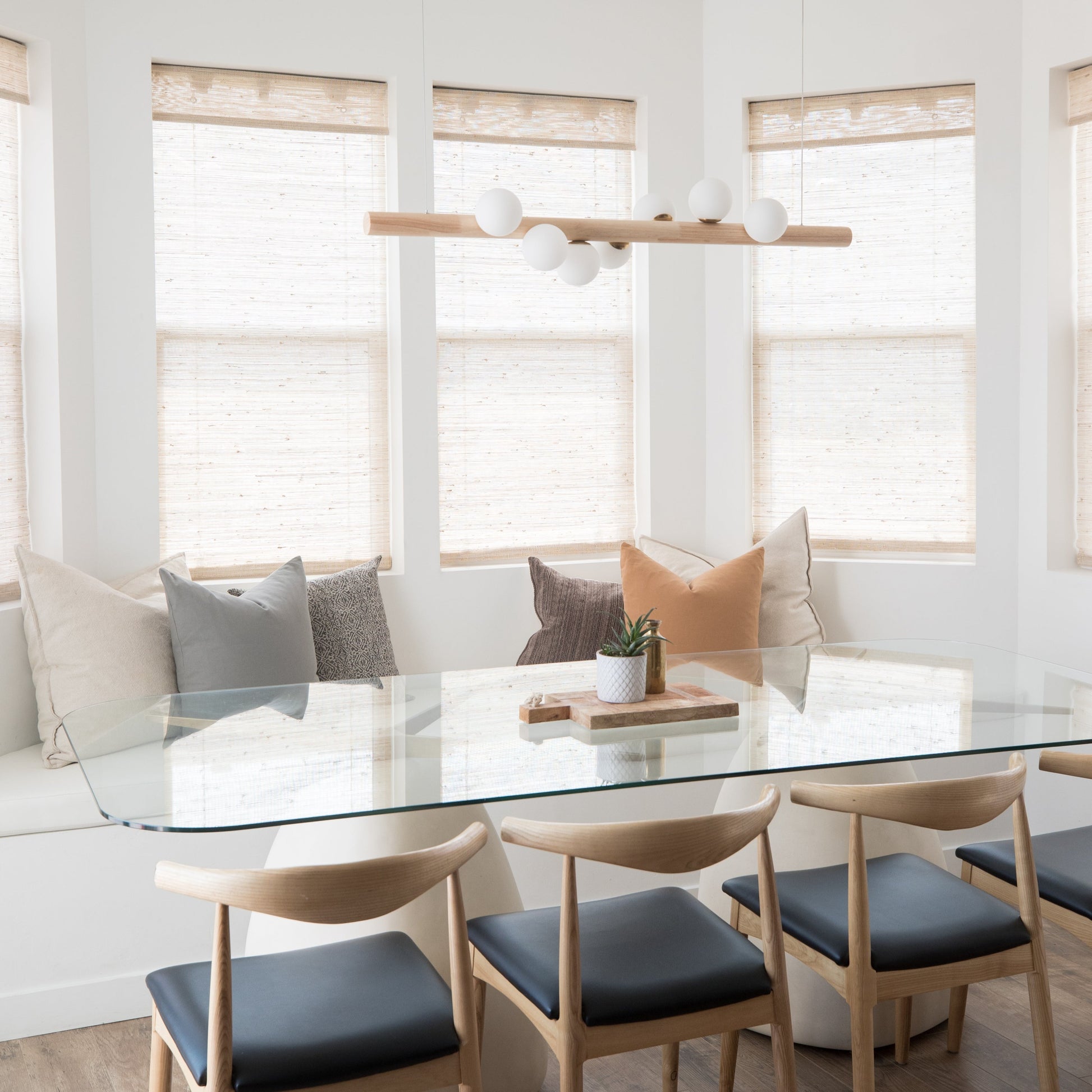 Linear pendant with natural wood bar and white spherical shades suspended above dining table.