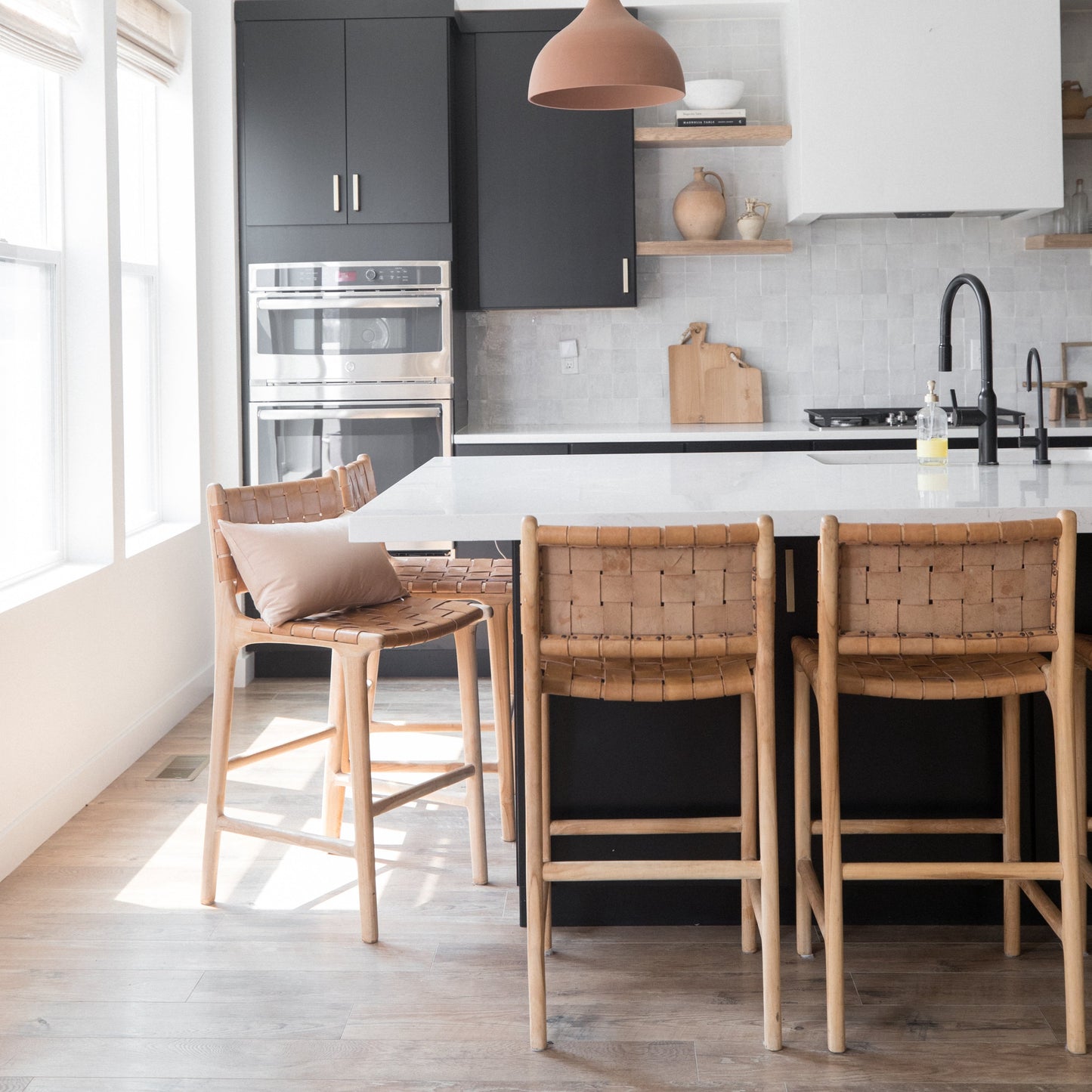 Woven leather bar stools with wooden frames positioned at a kitchen island counter.