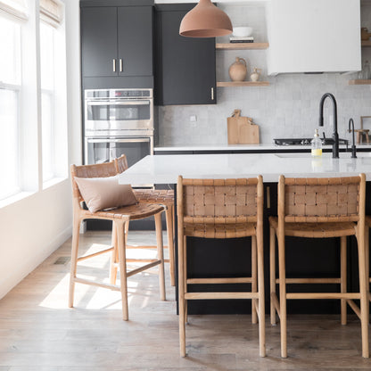 Woven leather bar stools with wooden frames positioned at a kitchen island counter.