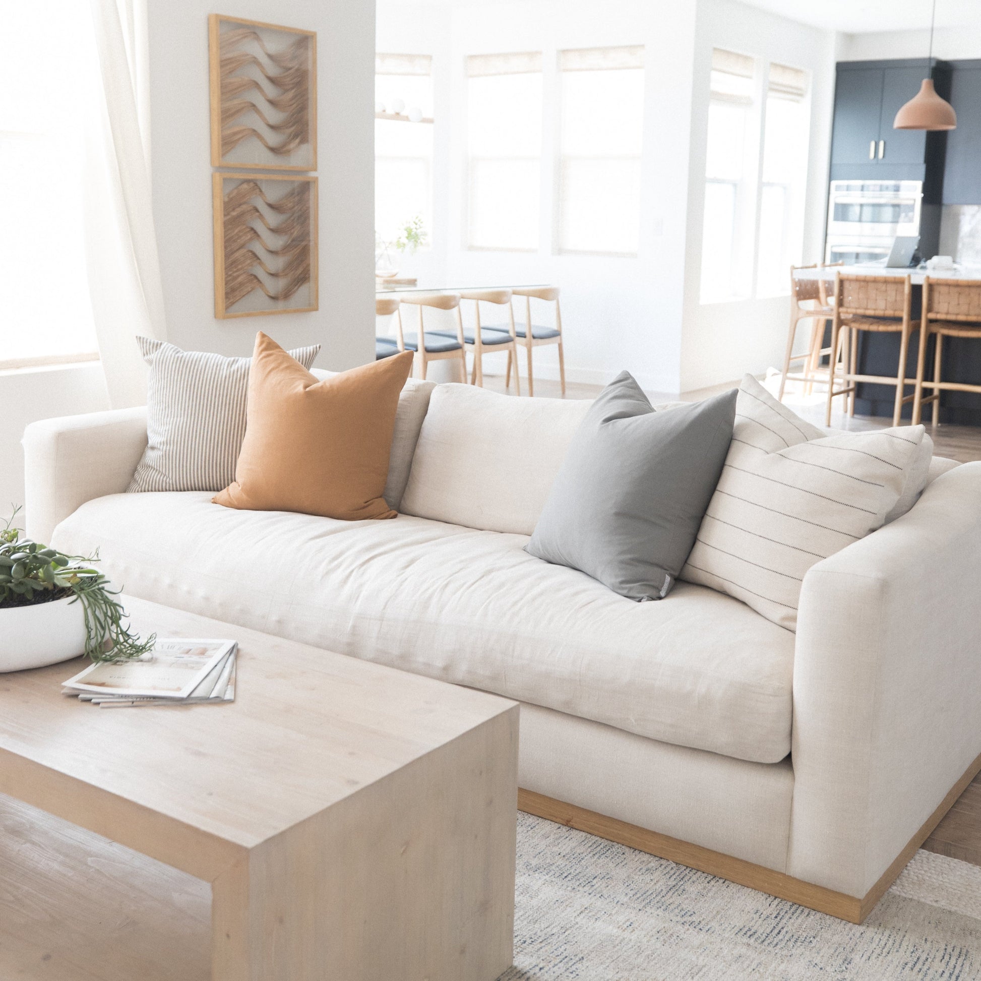 Cream upholstered sofa with wood base, styled with tan, gray, and striped pillows in a bright living room.