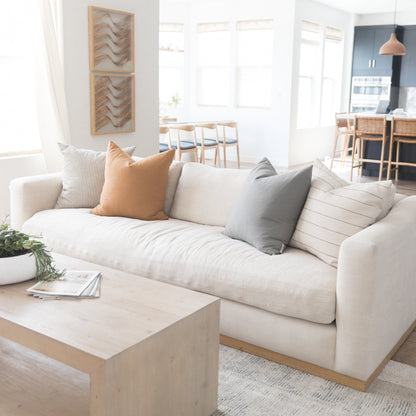 Cream upholstered sofa with wood base, styled with tan, gray, and striped pillows in a bright living room.