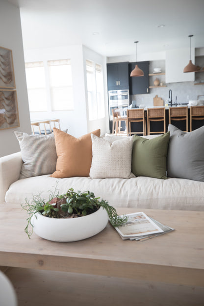 Cream sofa styled with striped, tan, cream, olive, and gray throw pillows in a bright living room.