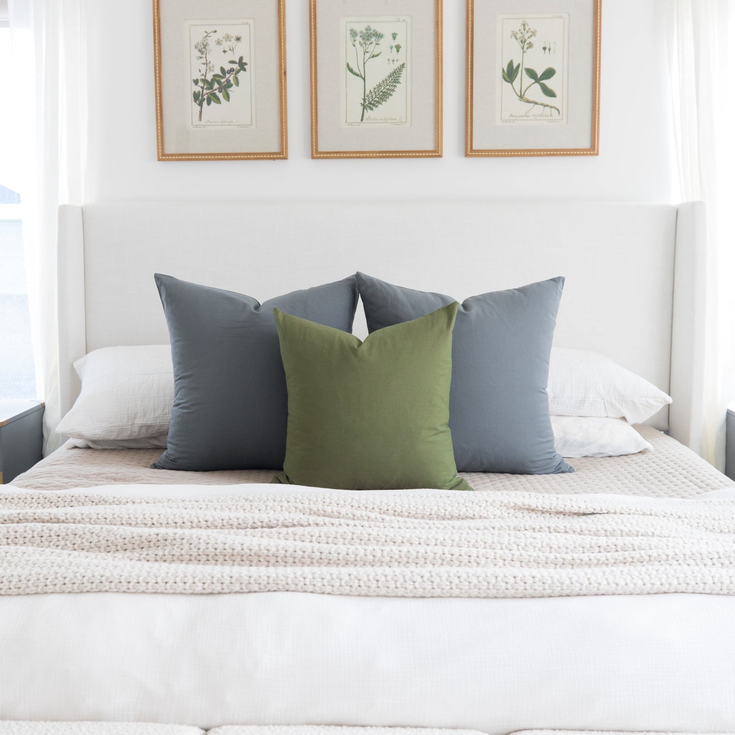 Olive green and slate blue throw pillows arranged on a bed with white headboard and bedding.