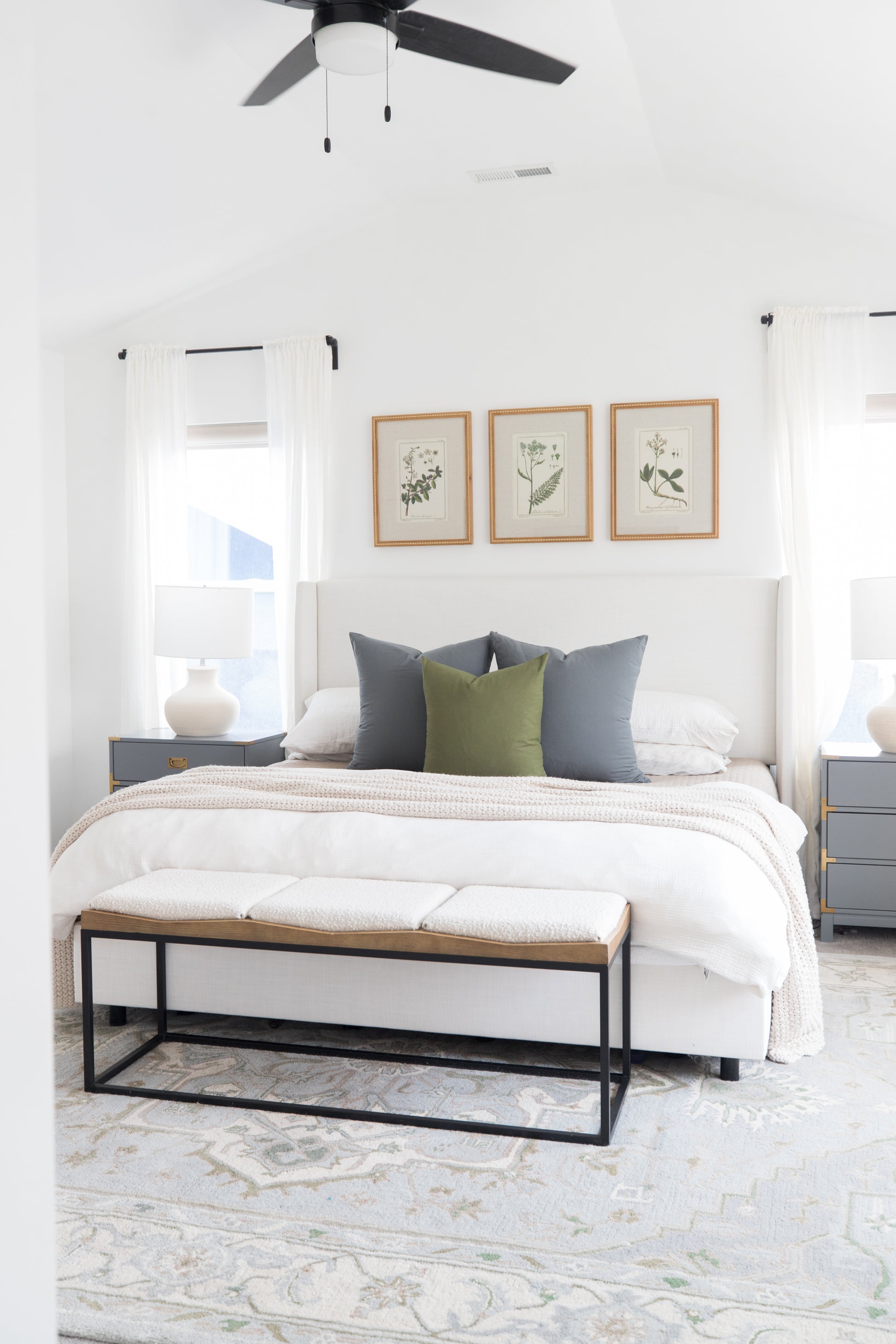 Olive green throw pillow on a white bed with gray pillows in a bright bedroom.