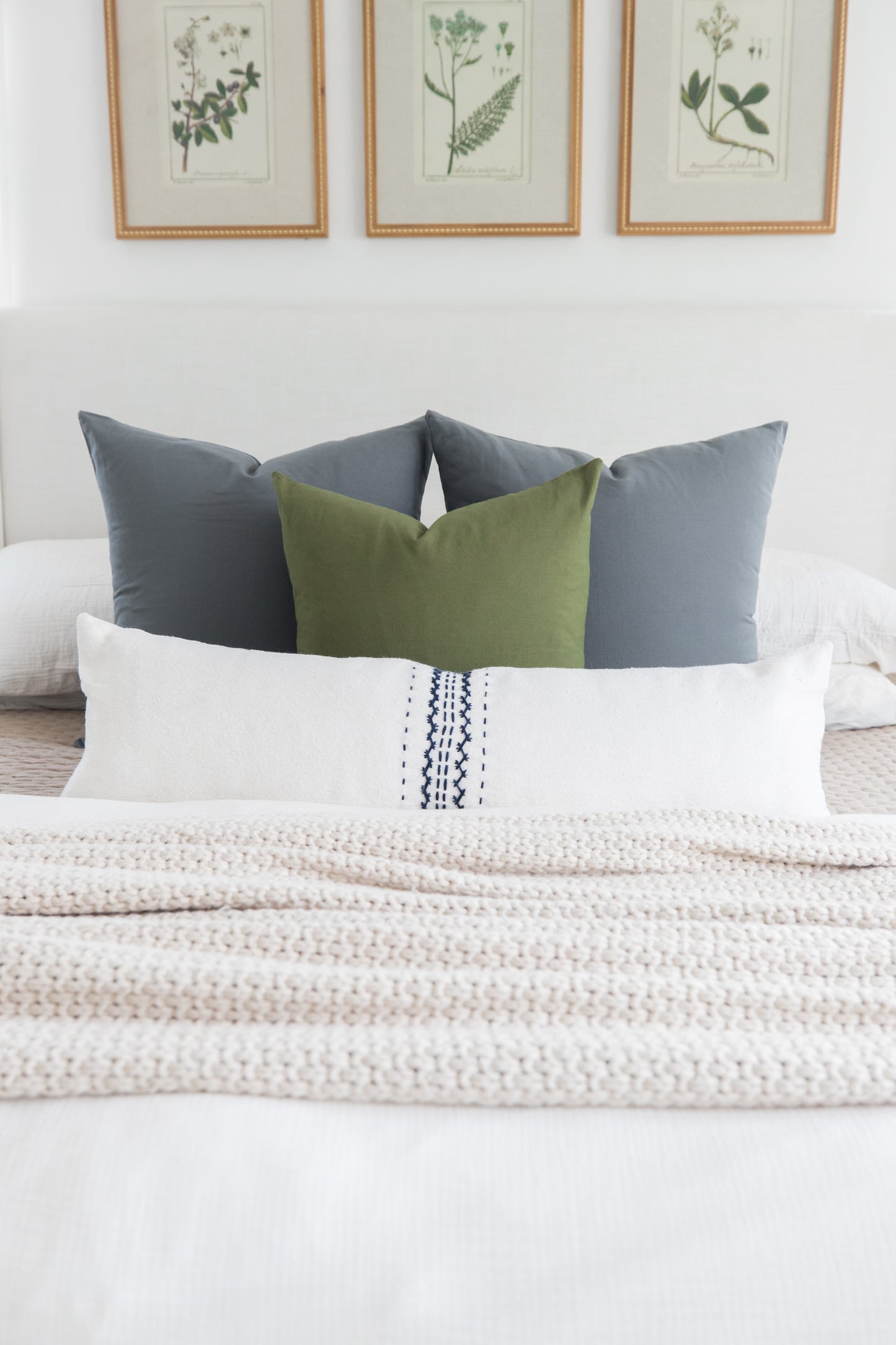 Bed styled with white lumbar pillow with navy stitching, olive and gray square pillows, and cream textured throw.