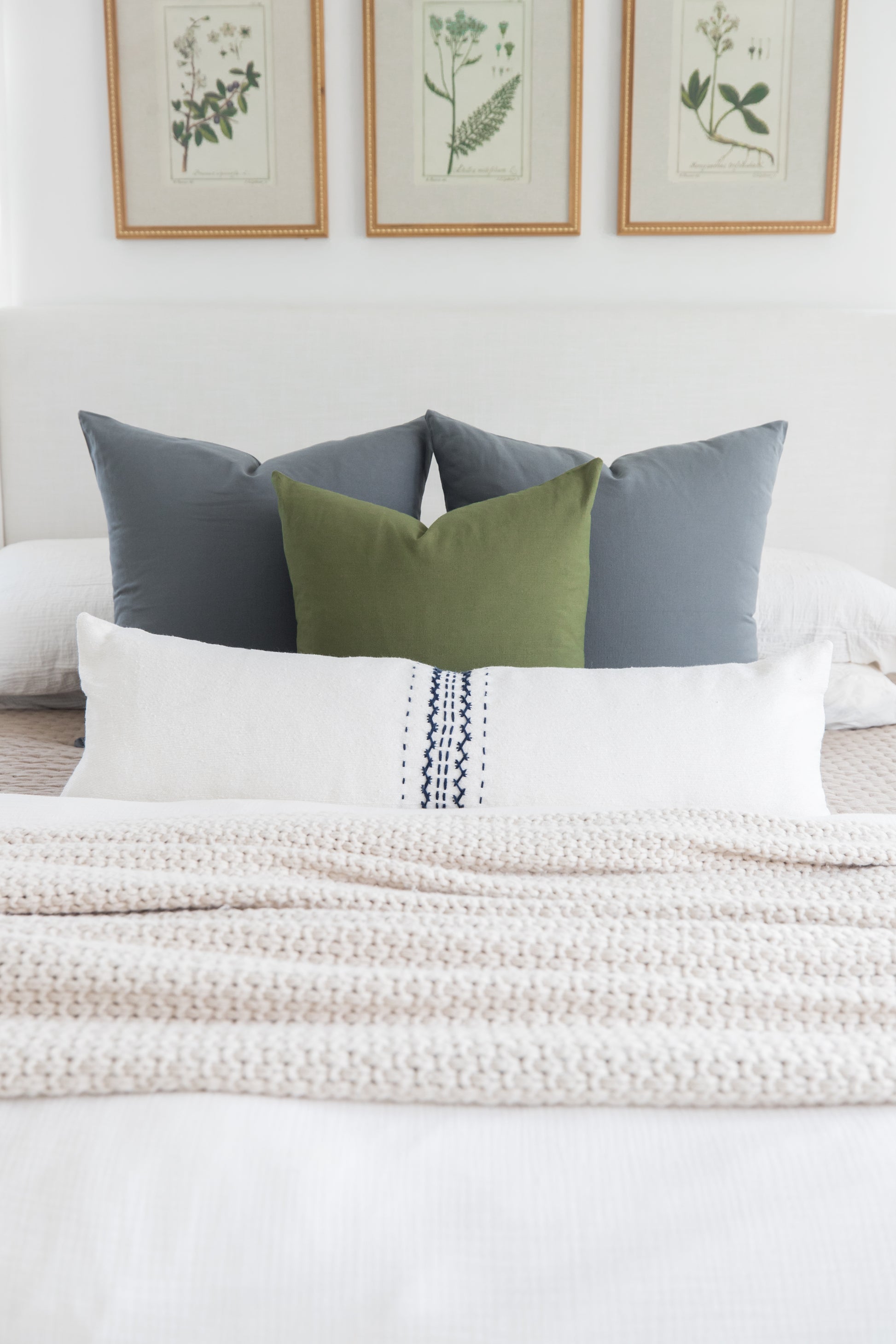 Bed styled with white lumbar pillow with navy stitching, olive and gray square pillows, and cream textured throw.