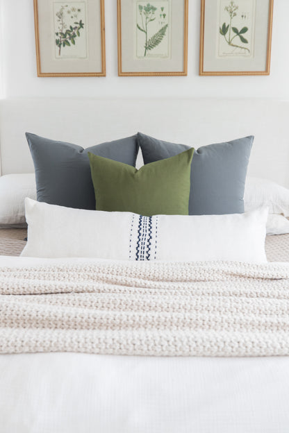 Bed styled with white lumbar pillow with navy stitching, olive and gray square pillows, and cream textured throw.