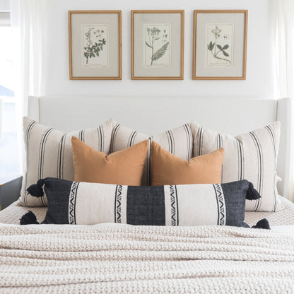 Bed styled with striped and solid terracotta pillows, patterned lumbar pillow, and three botanical framed prints above headbo