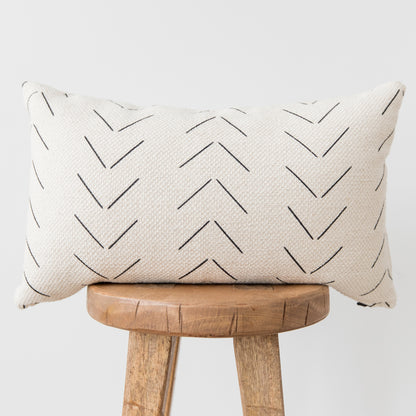 Cream lumbar pillow with black chevron pattern, displayed on wooden stool.