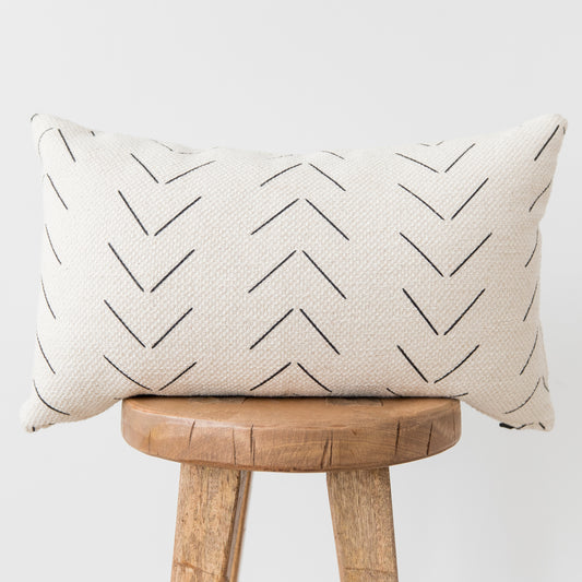 Cream lumbar pillow with black chevron pattern, displayed on wooden stool.