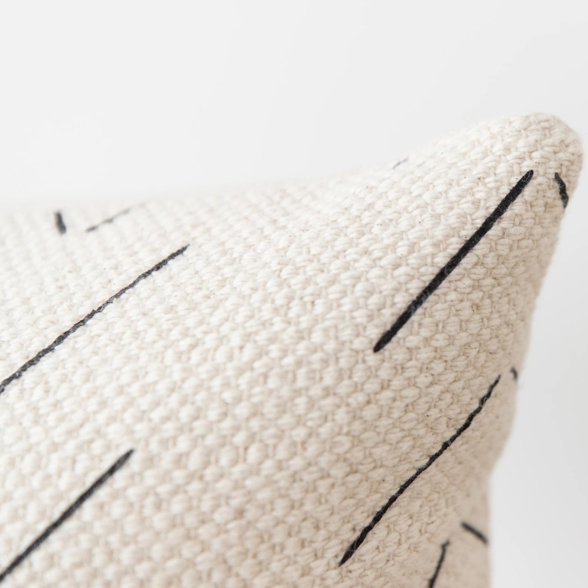 Cream-colored lumbar pillow with black linear stitch detailing on textured woven fabric.