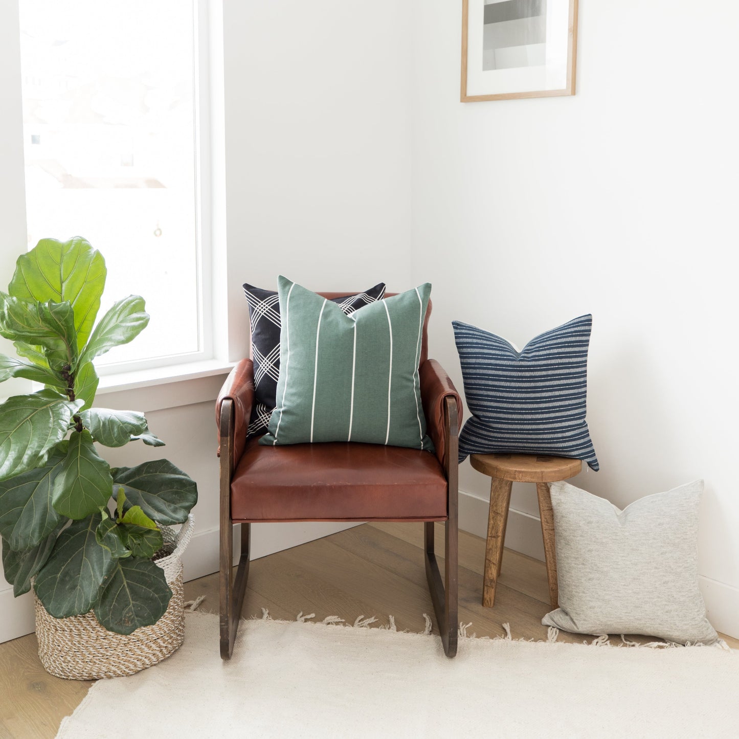 Green striped throw pillow with white lines displayed on a cognac leather chair with wooden arms.