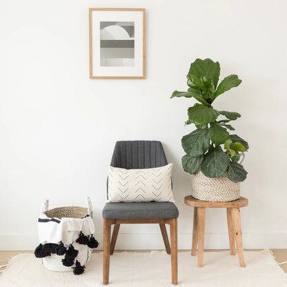 Cream lumbar pillow with chevron pattern displayed on wooden chair with gray cushion.