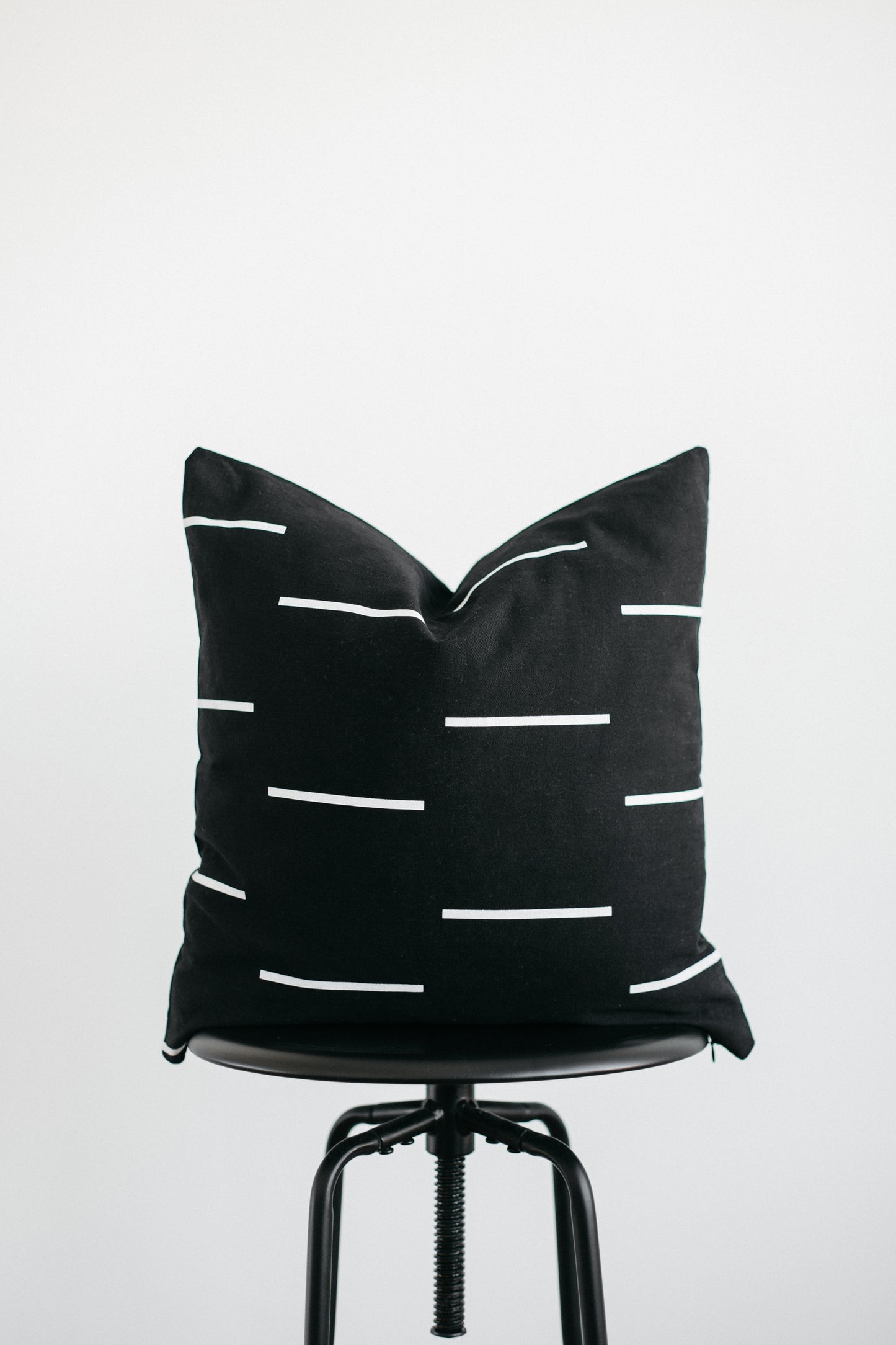 Black cushion with white horizontal stripes displayed on a stool against a light background.