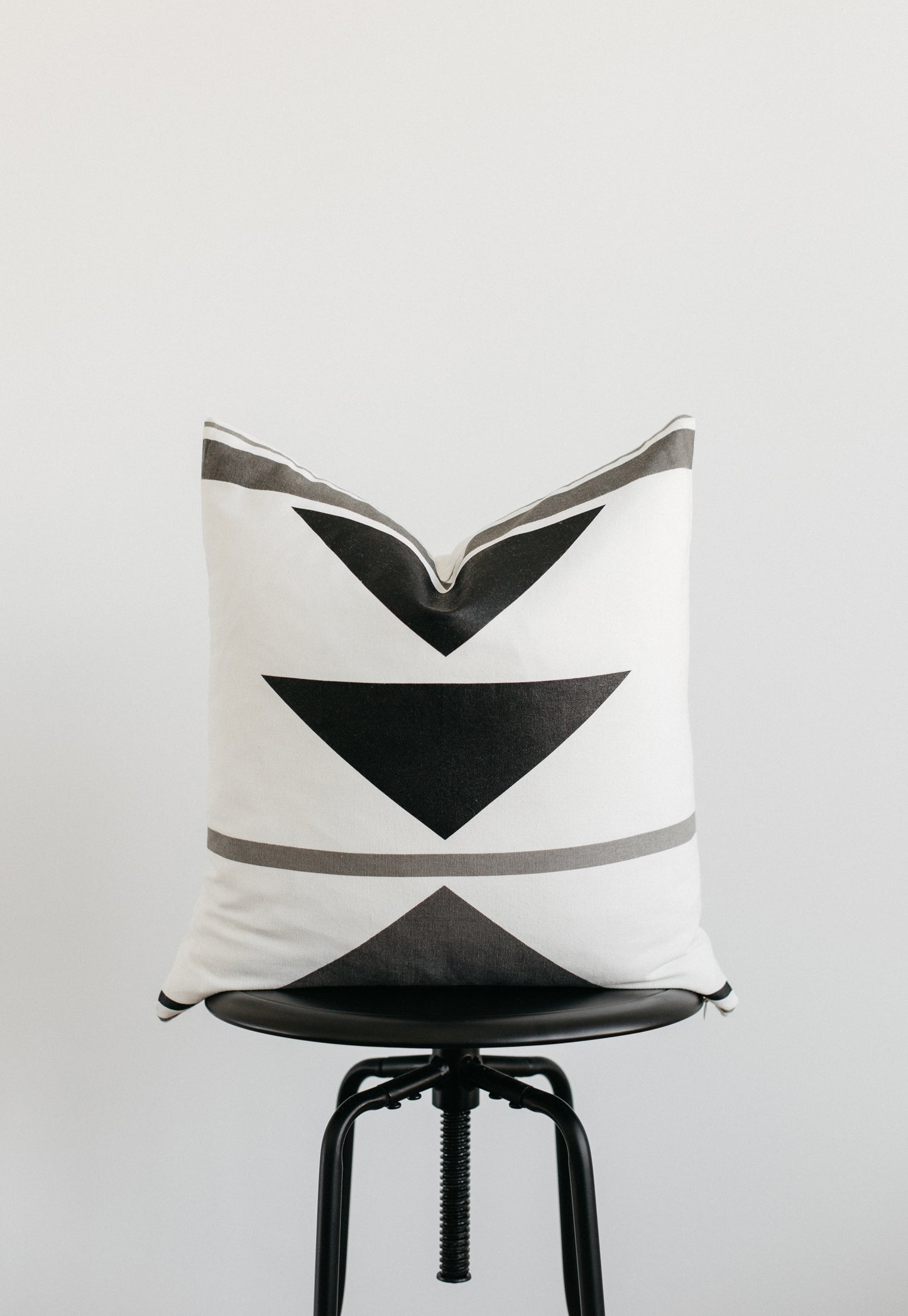 White linen pillow with black and gray geometric chevron pattern displayed on black chair.