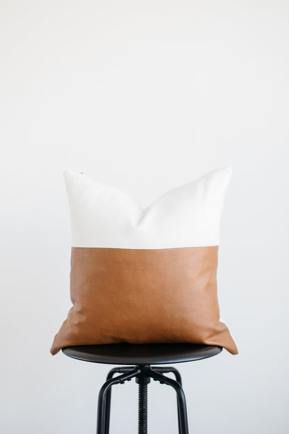 Rectangular pillow with white linen top half and tan leather bottom half, displayed on a black swivel stool.
