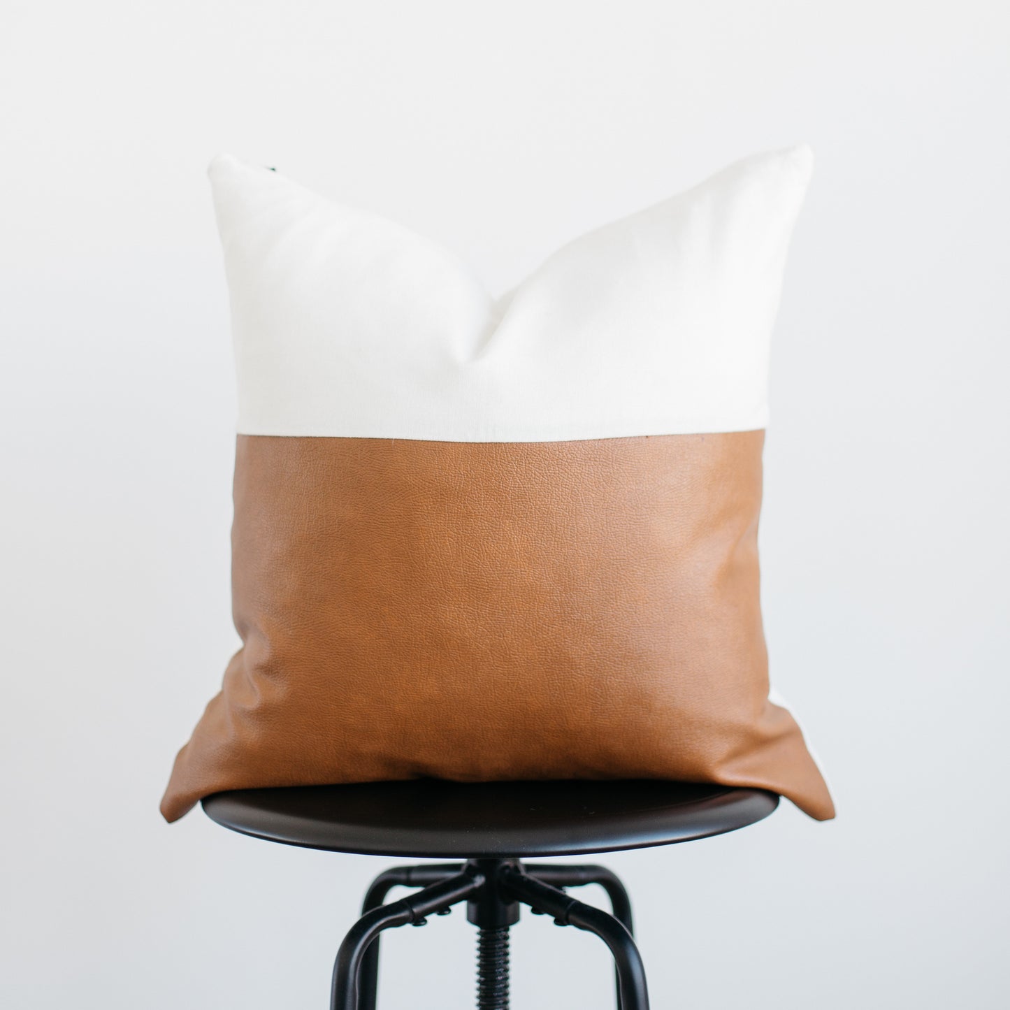 Decorative pillow with white linen upper half and tan leather lower half on black chair.