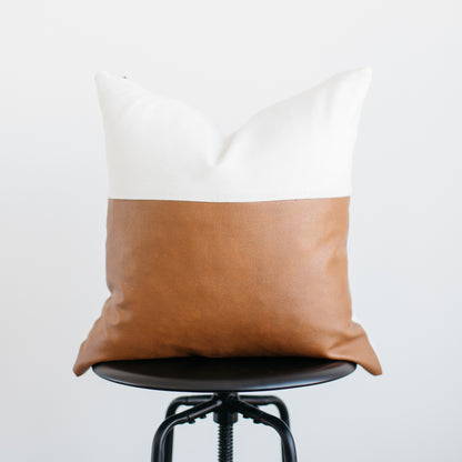 Decorative pillow with white linen upper half and tan leather lower half on black chair.