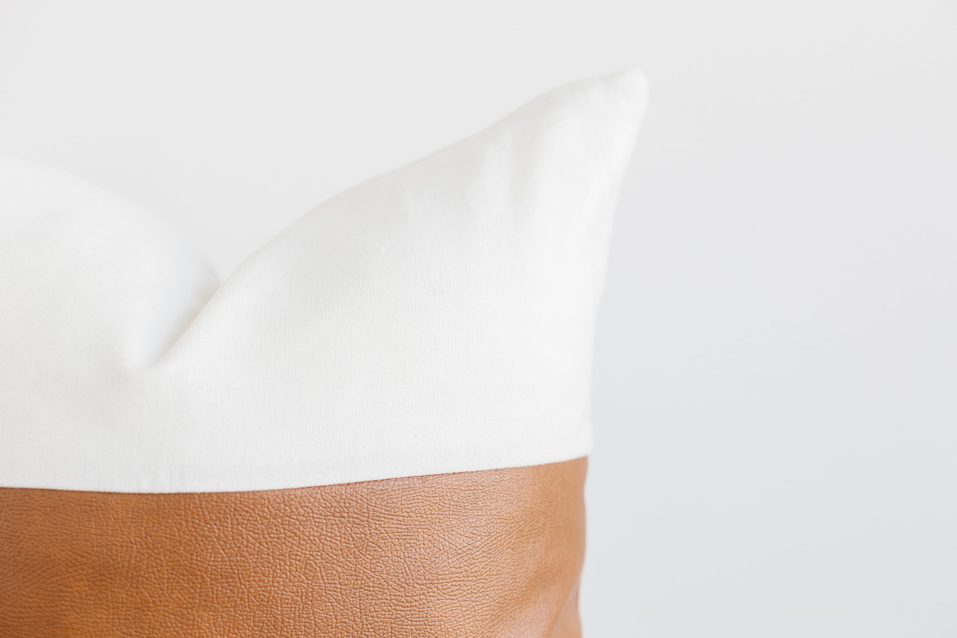 White pillow with tan leather base detail against neutral background.