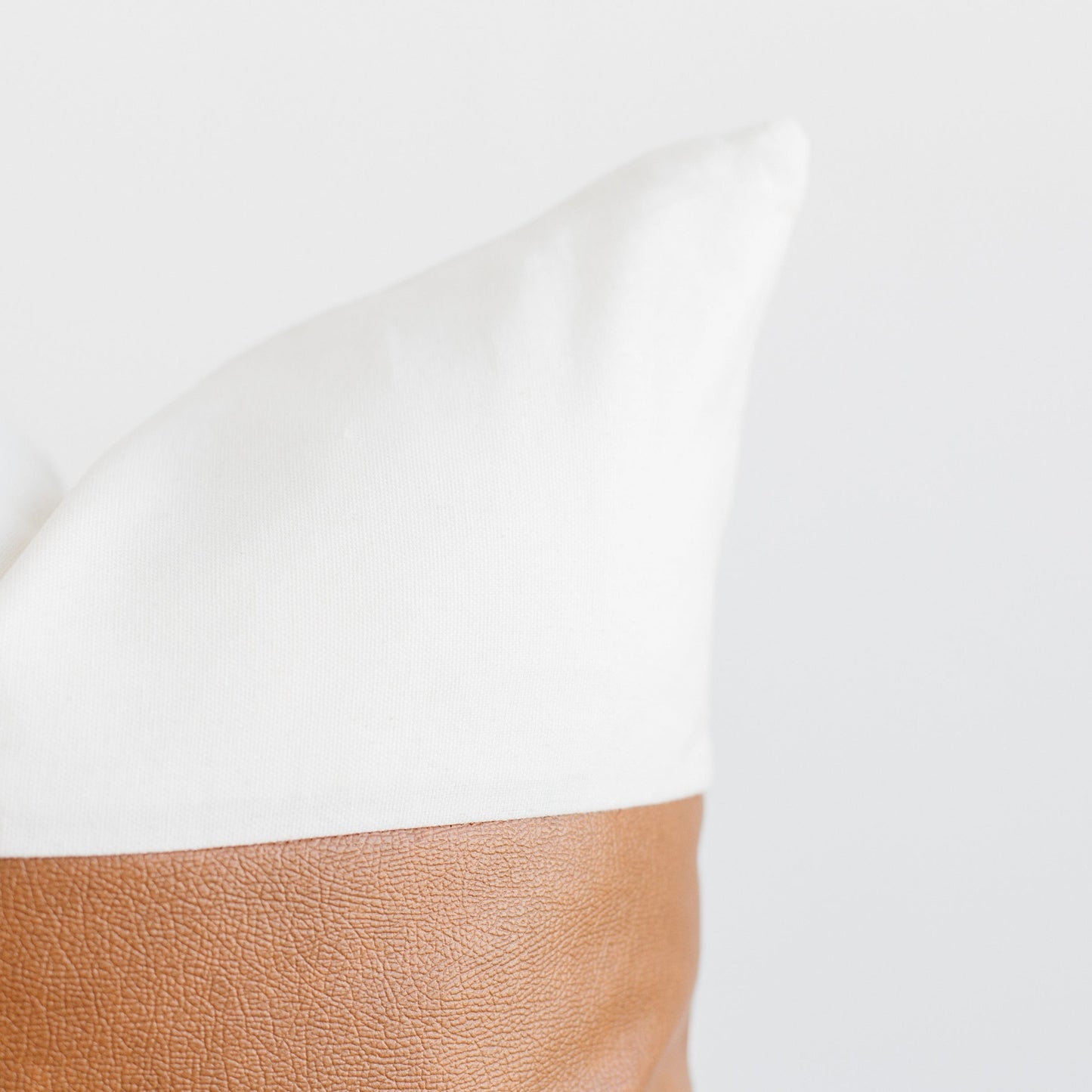 White pillow with tan leather base panel against neutral background.