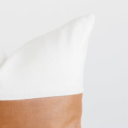 White pillow with tan leather base panel against neutral background.