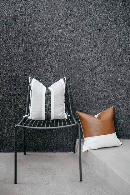 Black metal chair with white and gray striped pillow, brown leather pillow on concrete ledge against textured gray wall.