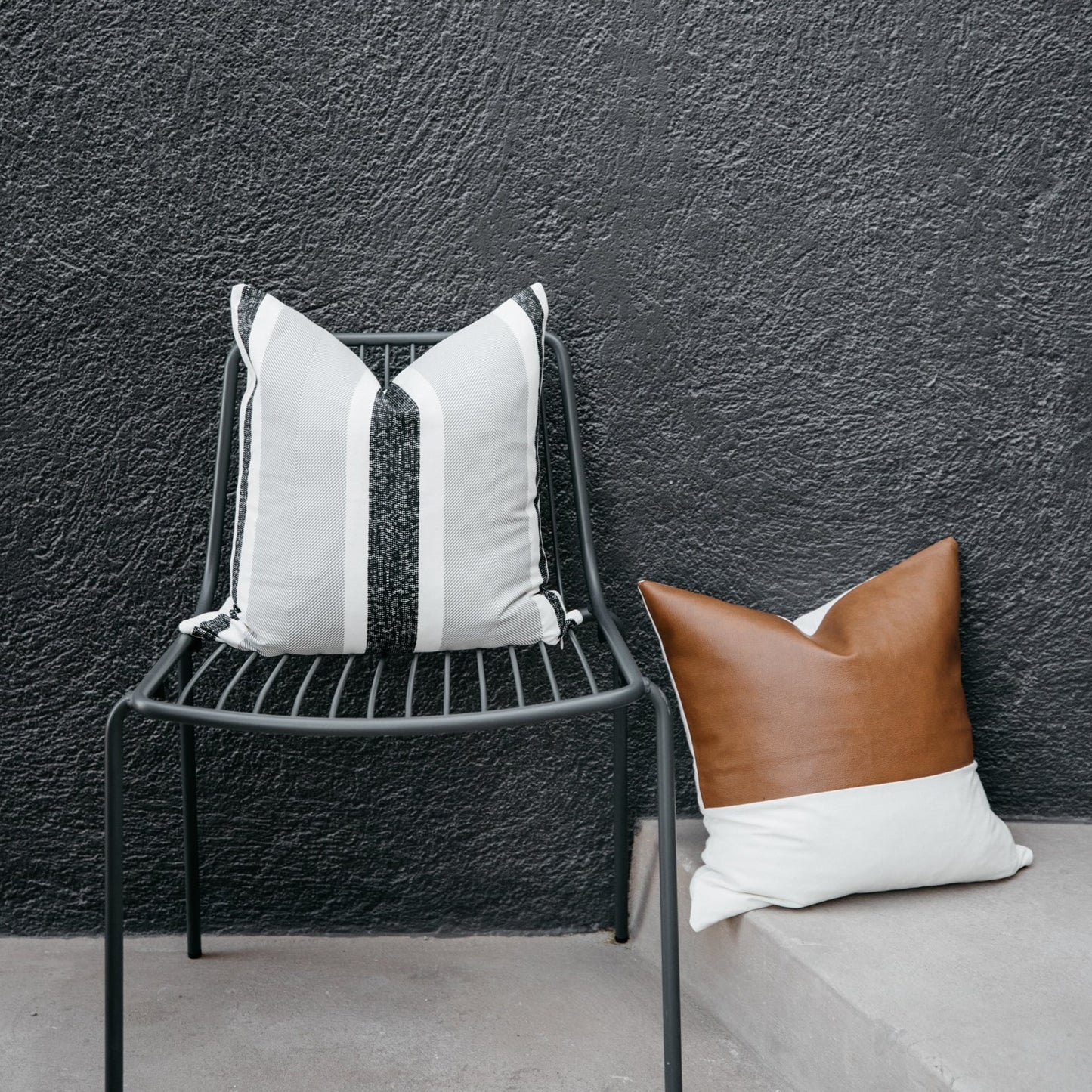 Black metal chair with vertical slat back design and white striped pillow against textured gray wall.