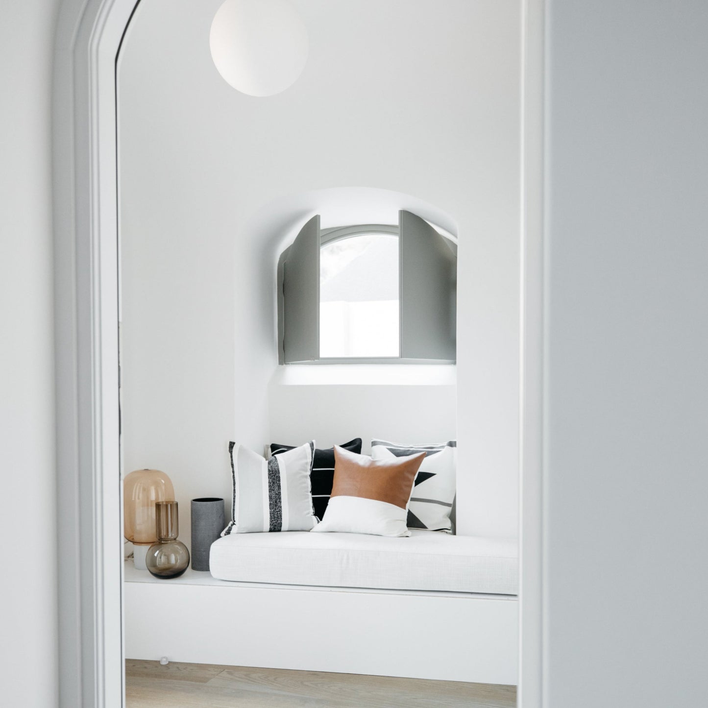 Arched mirror with brushed metal frame mounted above built-in bed with white mattress and patterned pillows.