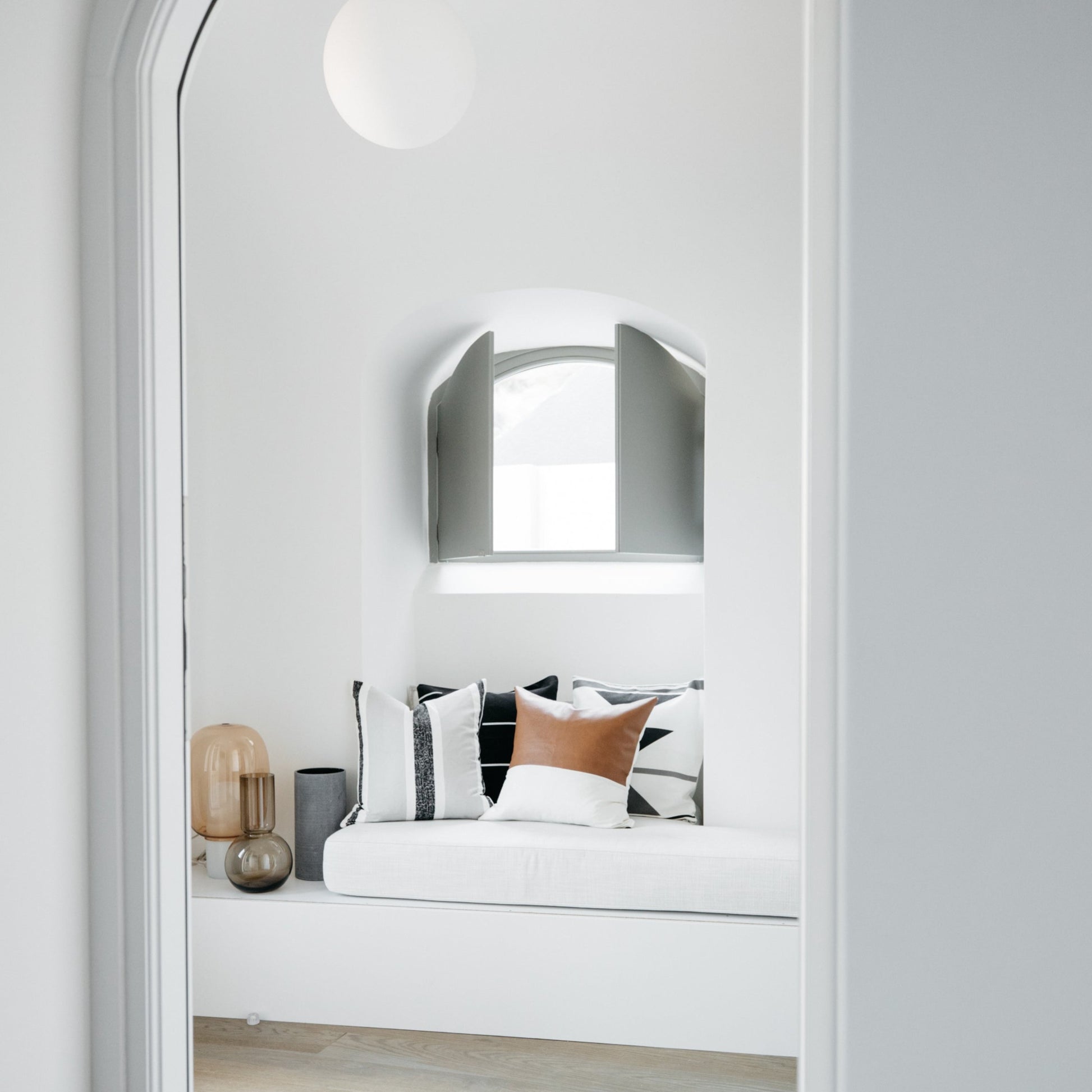 Arched mirror with brushed metal frame mounted above built-in bed with white mattress and patterned pillows.