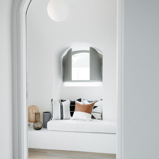Arched mirror with brushed metal frame mounted above built-in bed with white mattress and patterned pillows.