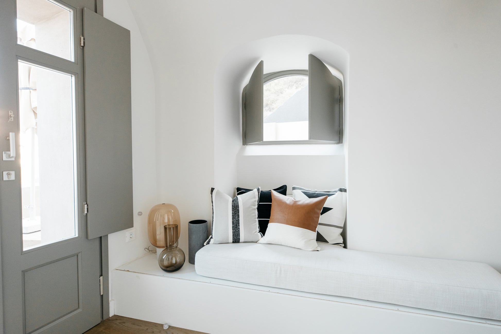 Arched silver-framed mirror mounted above white bed with patterned pillows in minimalist bedroom.