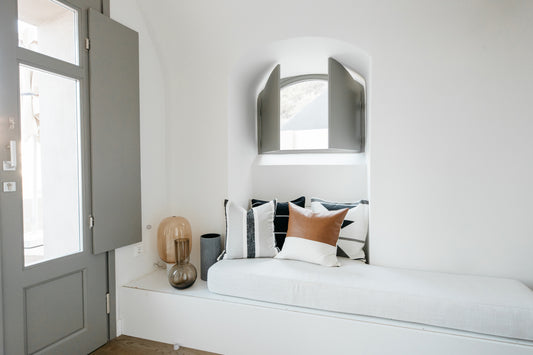 Arched silver-framed mirror mounted above white bed with patterned pillows in minimalist bedroom.