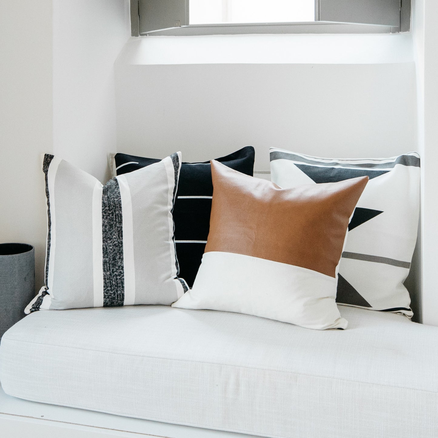 Four decorative pillows in varying sizes with striped, solid black, tan leather, and geometric patterns displayed on a white 