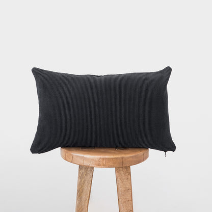 Dark gray corduroy lumbar pillow with ribbed texture displayed on a wooden stool.