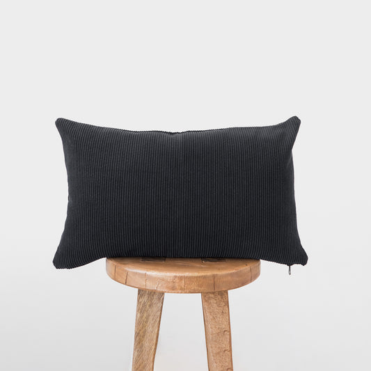 Dark gray corduroy lumbar pillow with ribbed texture displayed on a wooden stool.