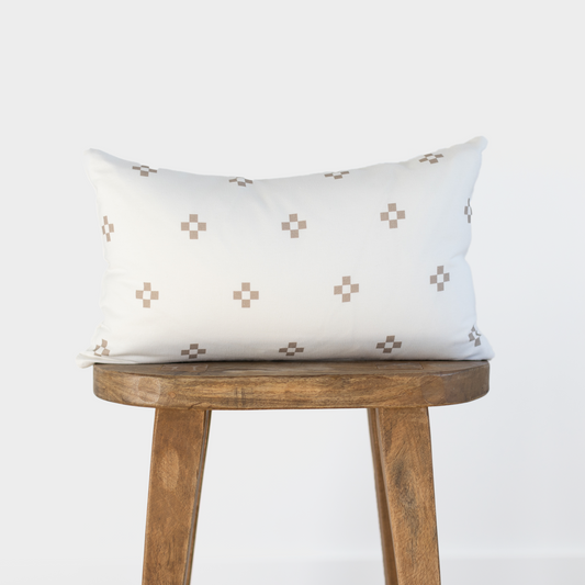 Cream lumbar pillow with tan square dot pattern displayed on wooden stool.