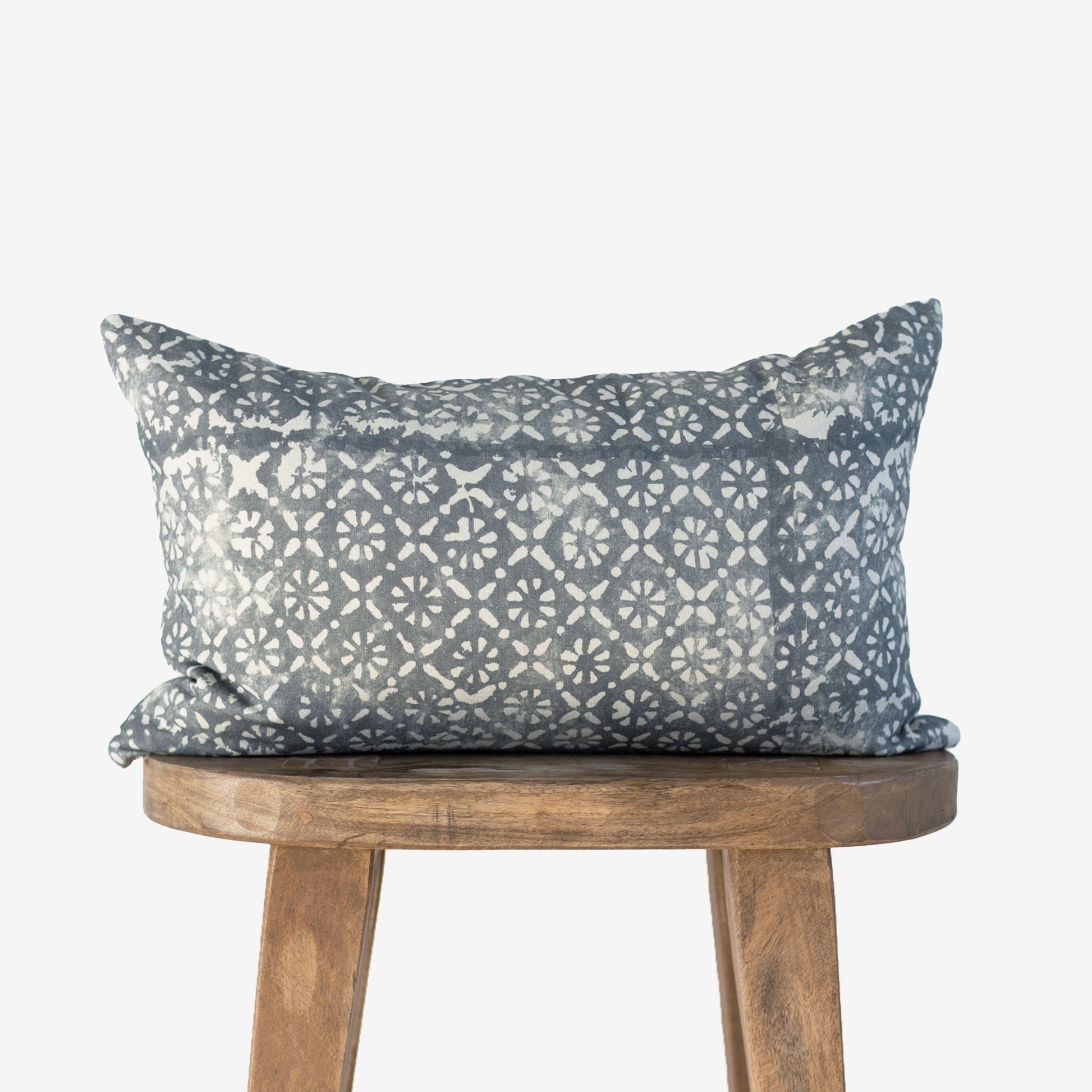 Gray lumbar pillow with cream diamond and floral geometric pattern, displayed on wooden stool.