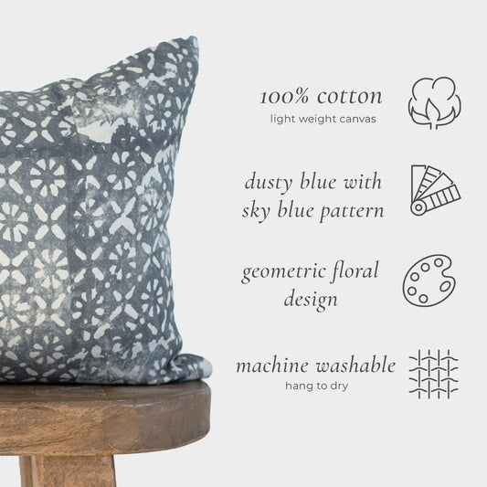 Rectangular lumbar pillow in dusty blue cotton with geometric floral pattern in sky blue, displayed on wooden stool.