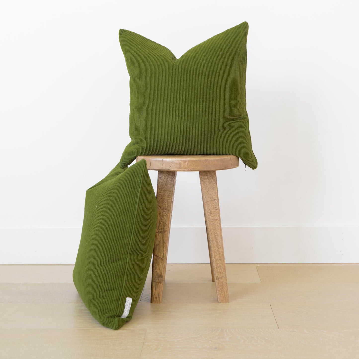 Two olive green corduroy pillows with ribbed texture displayed on a wooden stool.