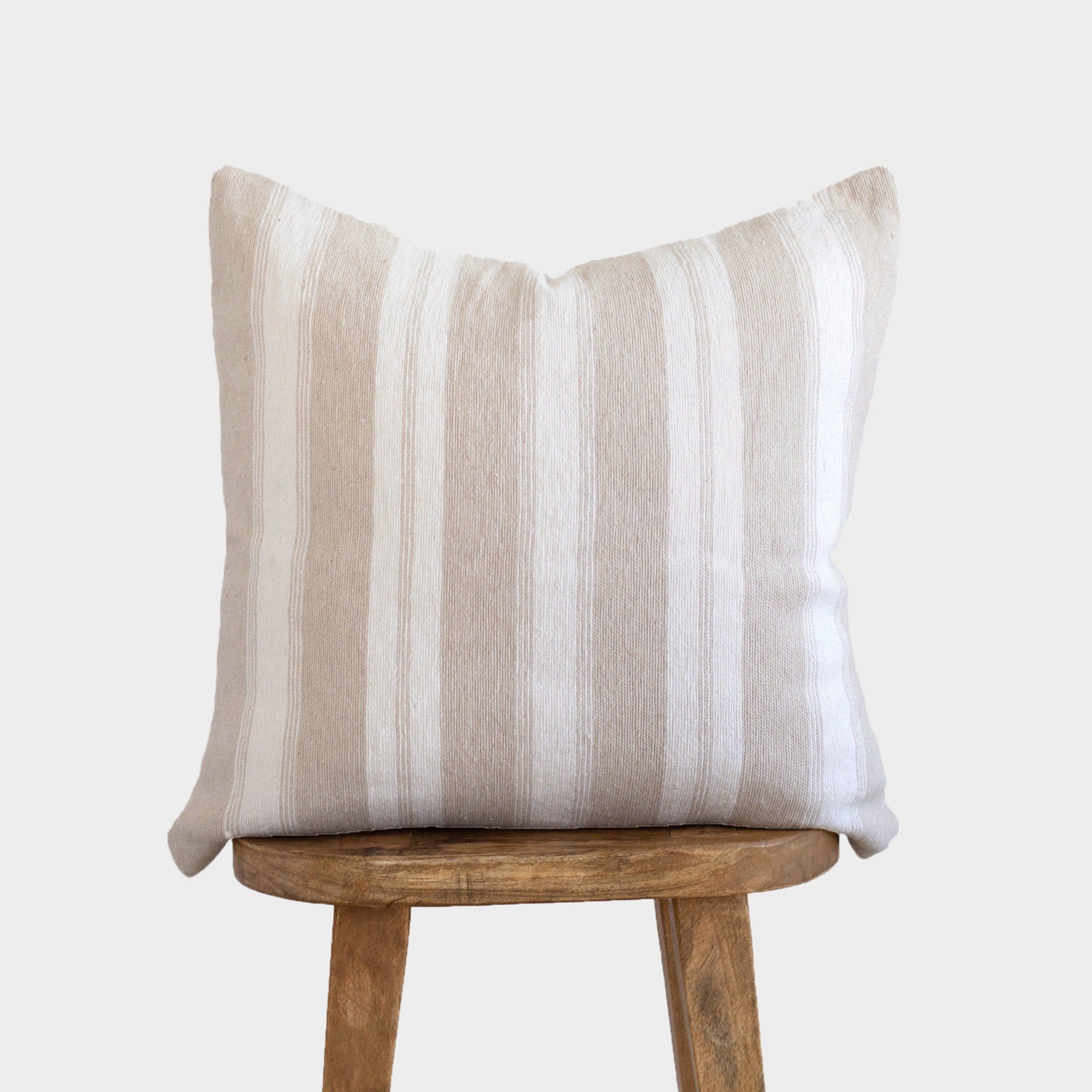 Tan and white striped throw pillow displayed on wooden stool.