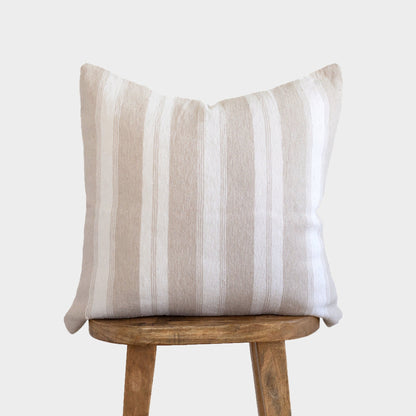Tan and white striped throw pillow displayed on wooden stool.
