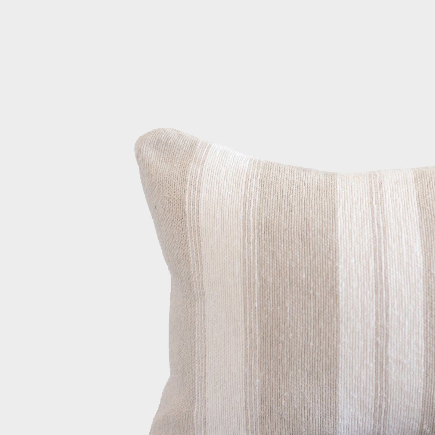Tan textured pillow with ribbed fabric surface and rounded corner detail against neutral background.