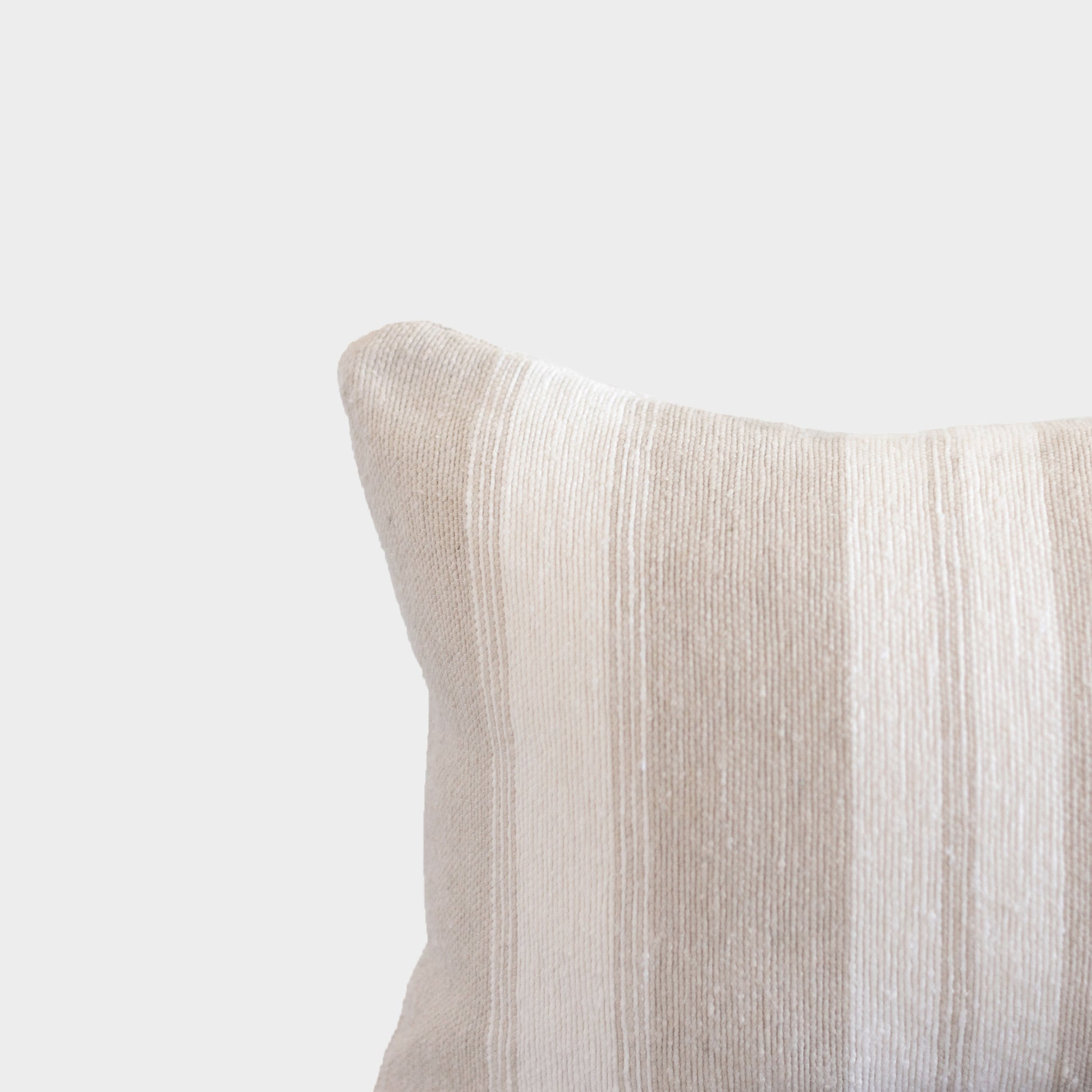 Tan textured pillow with ribbed fabric surface and rounded corner detail against neutral background.