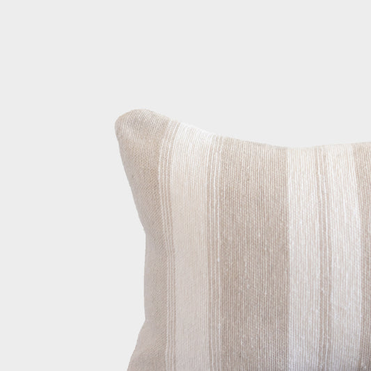 Tan textured pillow with ribbed fabric surface and rounded corner detail against neutral background.
