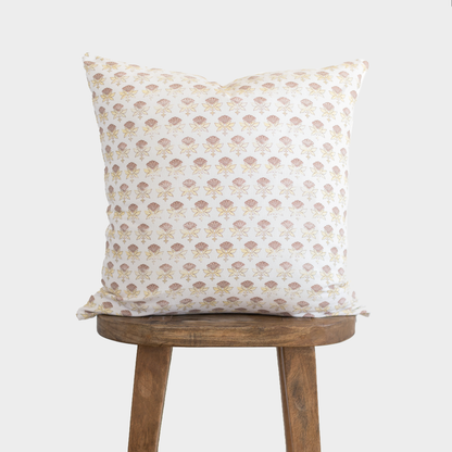 White pillow with tan floral fan pattern displayed on wooden stool.