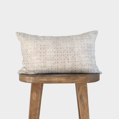 Cream-colored lumbar pillow with geometric grid pattern displayed on a wooden stool.