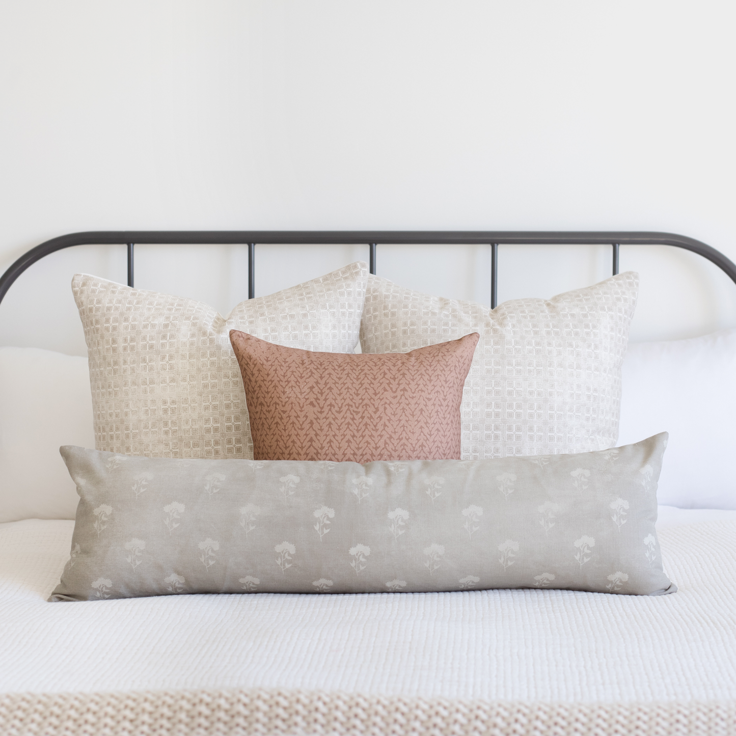 Gray lumbar pillow with white floral pattern displayed on bed with coordinating pillows.