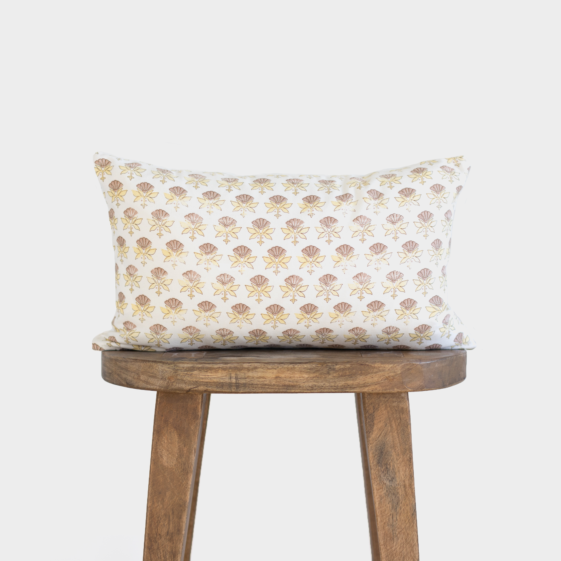 White lumbar pillow with tan and gold fan-shaped floral pattern, displayed on wooden stool.