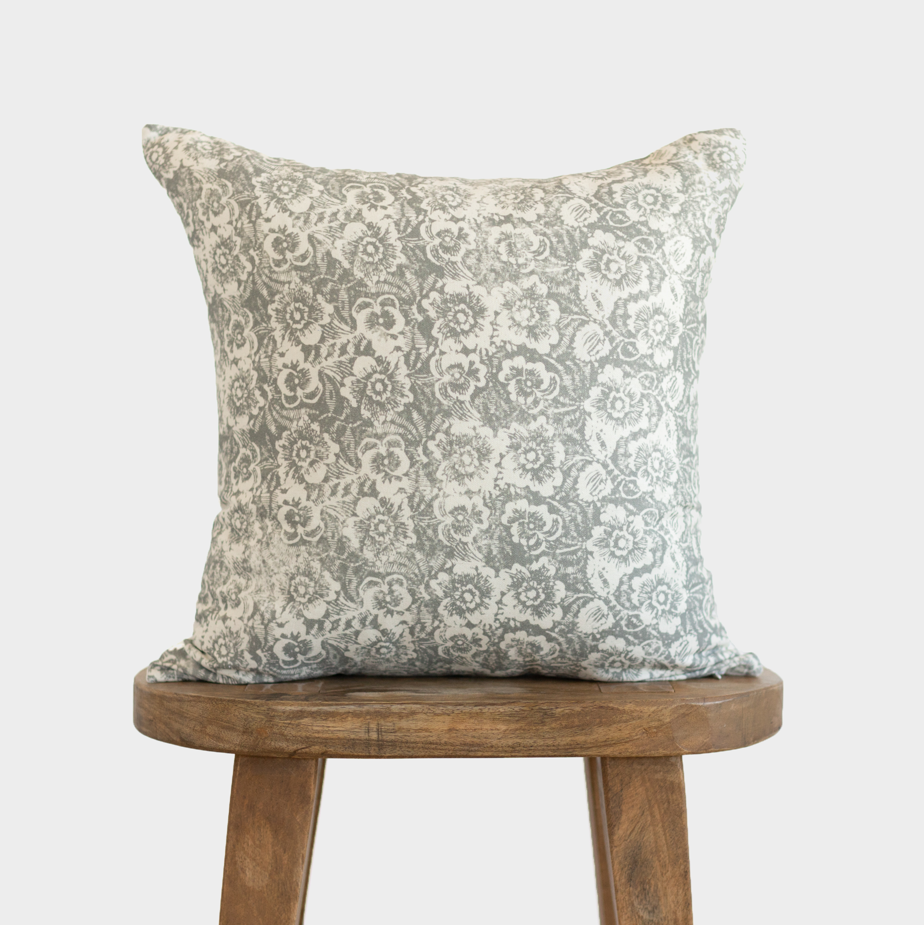 Gray and white floral patterned throw pillow displayed on a wooden stool.